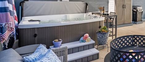 Un espace extérieur accueillant avec un coin salon, un jacuzzi, un barbecue et un foyer.