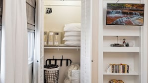 Een keurig opgeruimde slaapkamer met een bed, een aan de muur bevestigde televisie en een inbouwkast met planken.