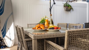 Een eettafel met rieten stoelen, een surfplank en een fles champagne.