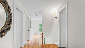 A hallway with wooden flooring, white walls, and a large ornate mirror on the left. - Spacious Riverfront Home 7 Minutes to Stratton! (Jamaica)