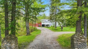 A rural road leading to a white house with a red barn, surrounded by trees and stone walls. - Spacious Riverfront Home 7 Minutes to Stratton! (Jamaica)