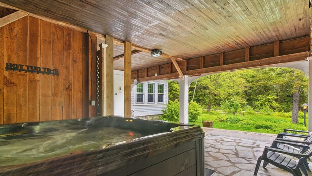 A hot tub under a wooden pergola with a view of a green landscape. - Spacious Riverfront Home 7 Minutes to Stratton! (Jamaica)