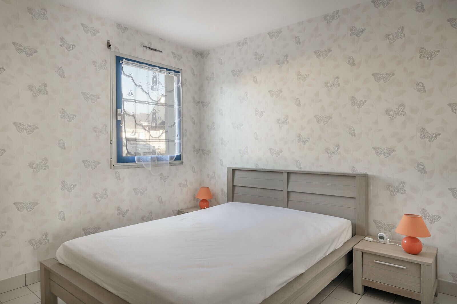 A bedroom with a bed, a nightstand, a lamp, and a window with a view of buildings.