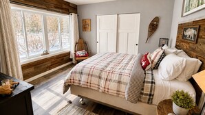 Un dormitorio con cama, mesita de noche, ventana y estante en la pared.