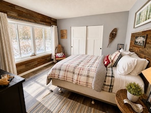 Een slaapkamer met een bed, nachtkastje, raam en een wandplank.