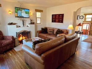 A living room with a leather sofa, a fireplace, a television mounted on the wall, and a lamp. - Historic Adobe Abode-Pet Friendly, Downtown Kanab (Kanab)