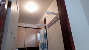 A narrow hallway with a shower area, a ceiling light, and a wooden door frame.