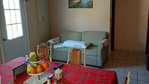 A dining area with a red plaid tablecloth, a bowl of fruit, and a sofa in the background.