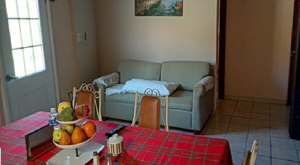 Zona pranzo con tovaglia a quadri rossi, una ciotola di frutta e un divano sullo sfondo.