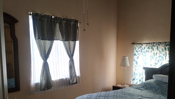 A bedroom with a bed, a window with curtains, a nightstand, and a lamp.