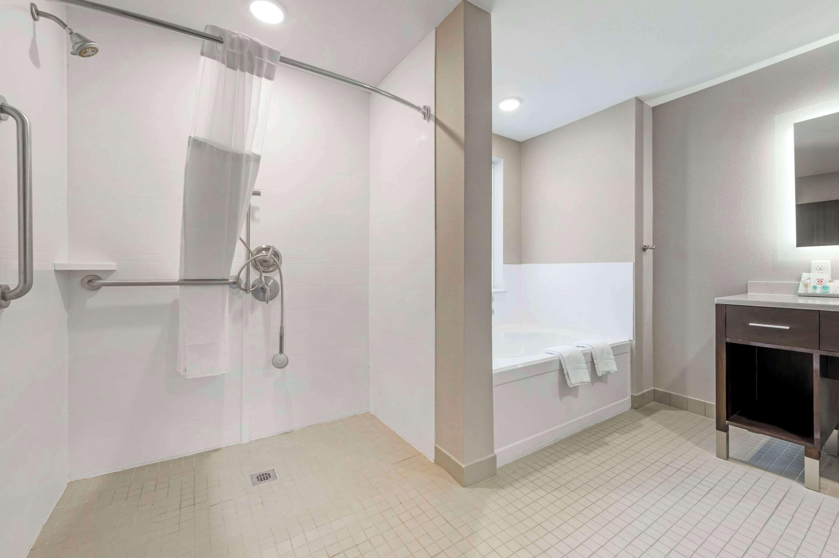 Ein modernes Badezimmer mit barrierefreier Dusche, einer Badewanne und einem Waschtisch mit Spiegel.