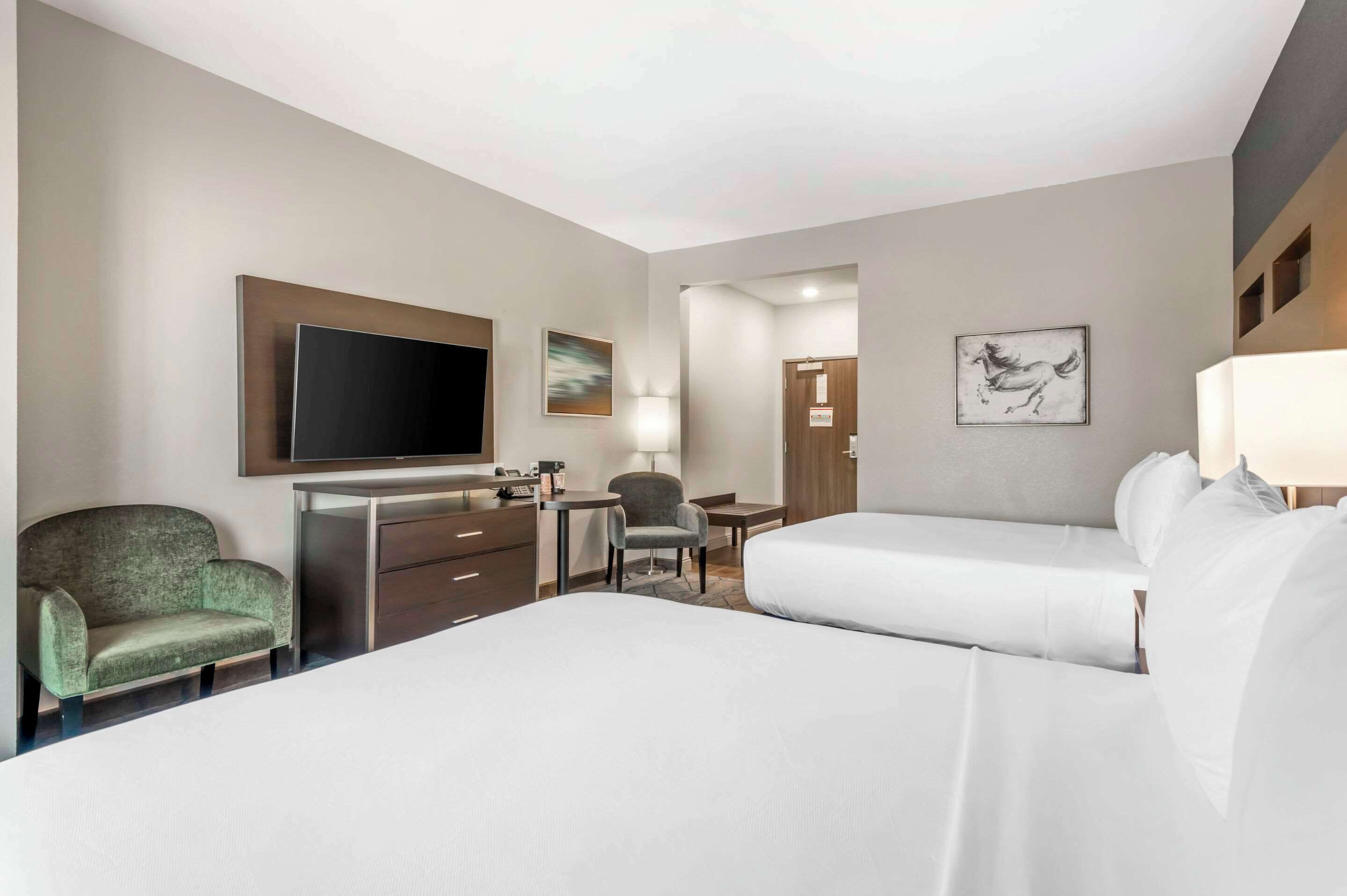 A hotel room with two beds, a desk, a chair, a TV, and artwork on the walls.