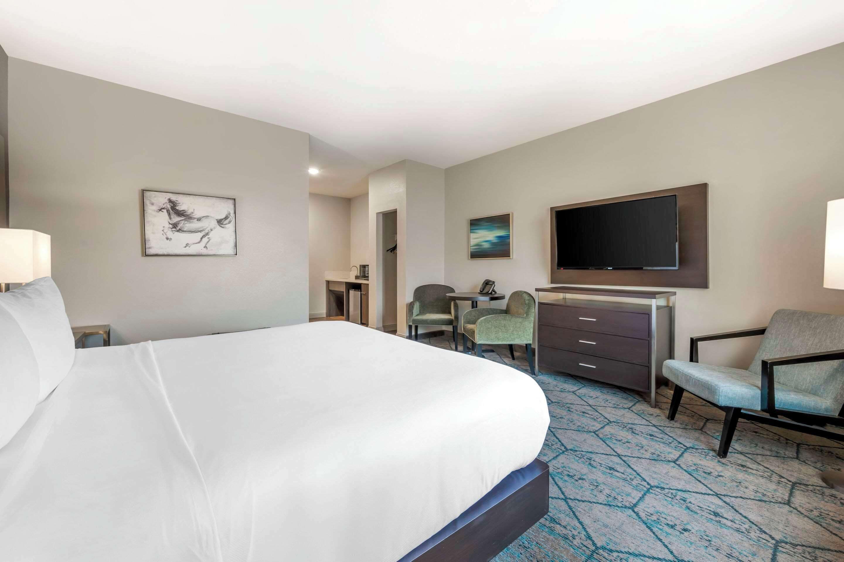 A hotel room with a large bed, a desk with a chair, a television, and artwork on the walls.