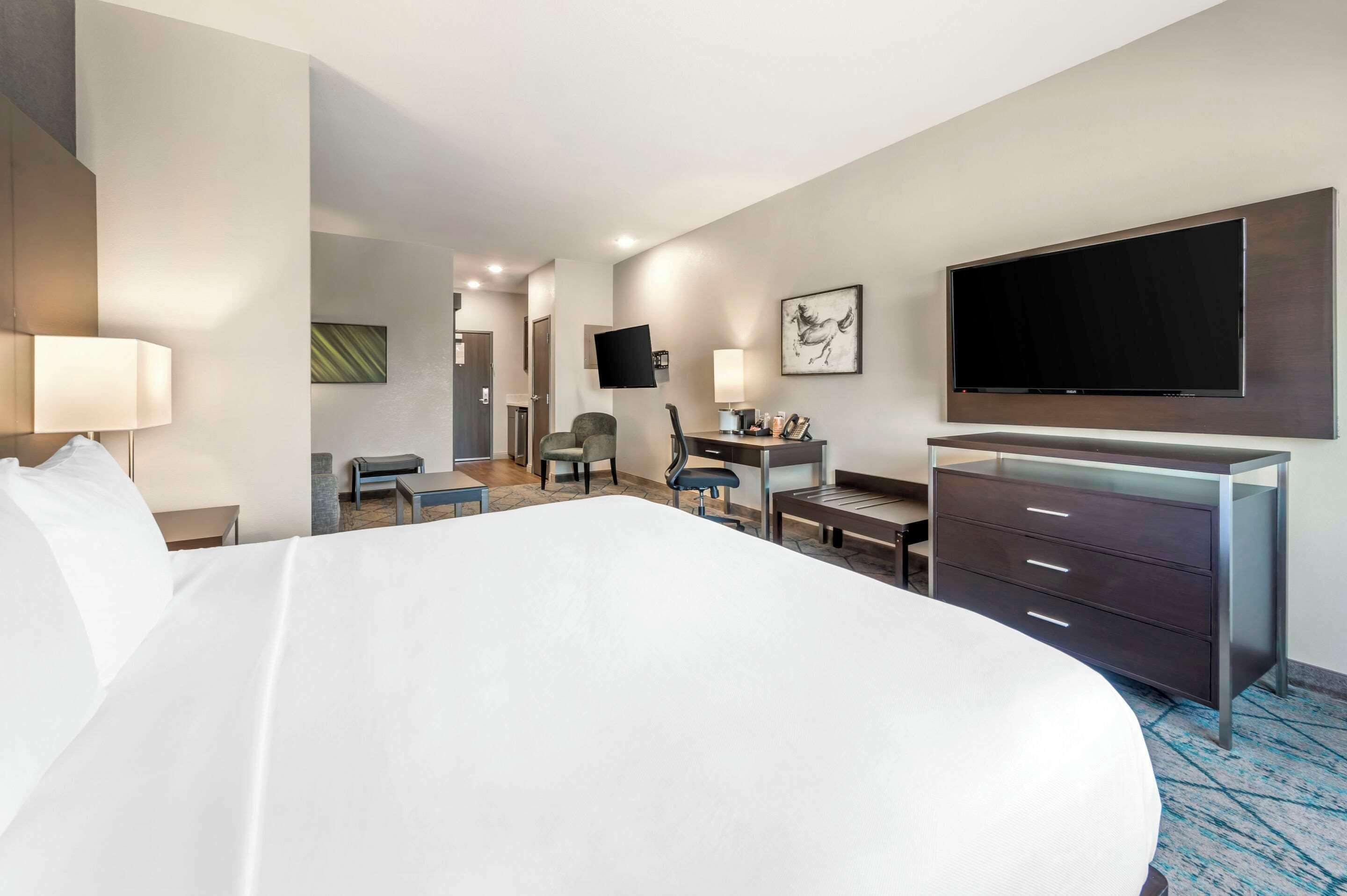 A hotel room with a large bed, a desk, a chair, a TV mounted on the wall, and a dresser.