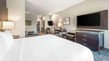 A hotel room with a large bed, a desk, a chair, a TV mounted on the wall, and a dresser.