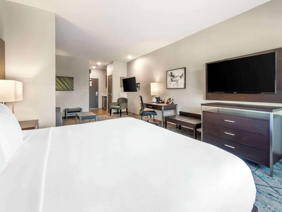 A hotel room with a large bed, a desk, a chair, a TV mounted on the wall, and a dresser.