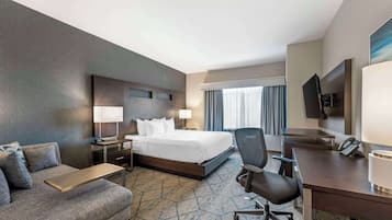 A hotel room with a bed, a desk, a chair, a sofa, a TV, and a window with curtains.