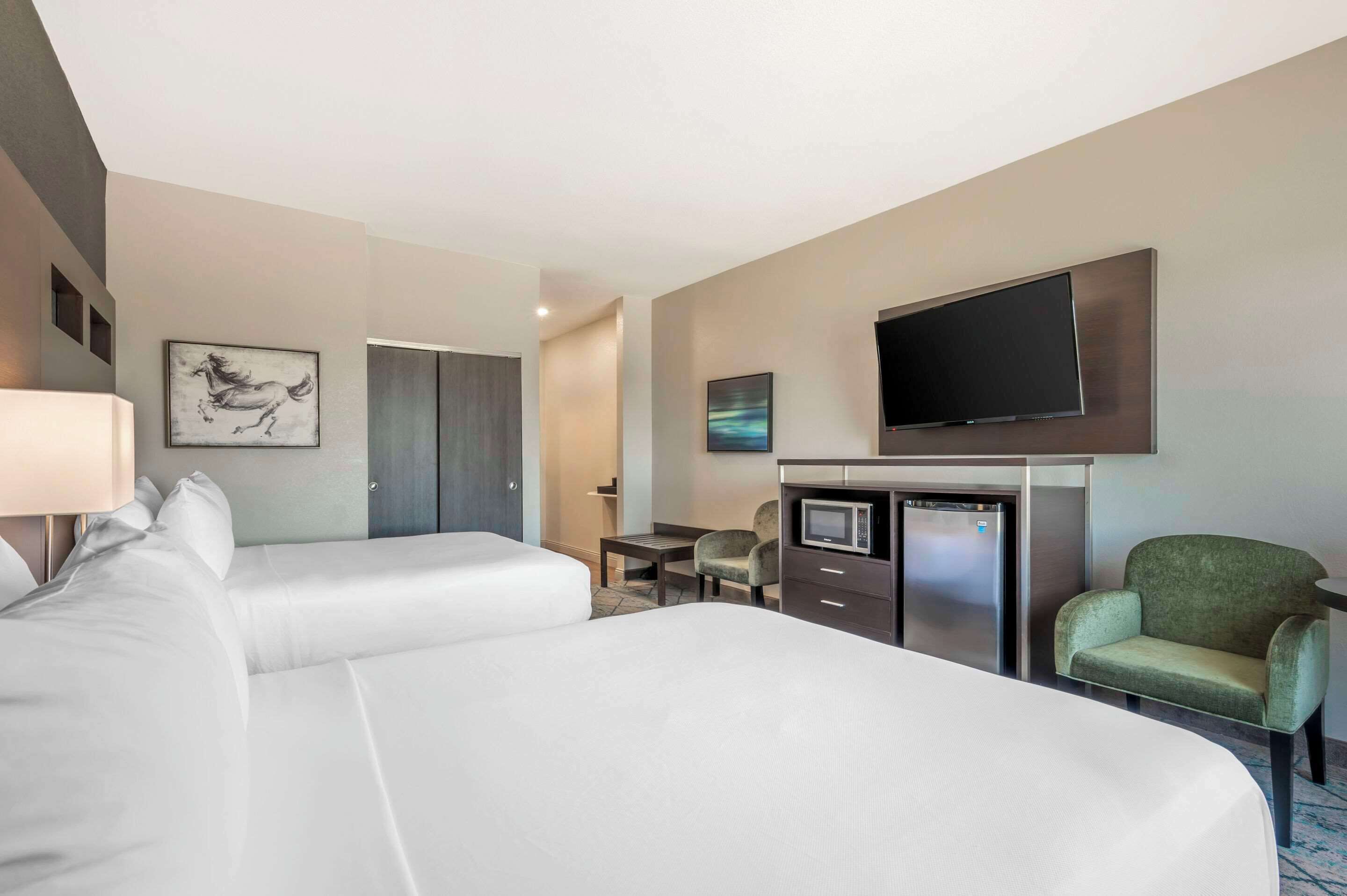 A hotel room with two beds, a flat-screen TV, a microwave, a small table, and a green armchair.