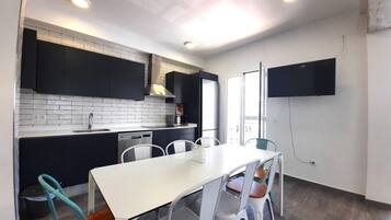Eine moderne Küche mit dunklen Schränken, einer weißen Arbeitsplatte und einem Essbereich mit weißem Tisch und Stühlen.