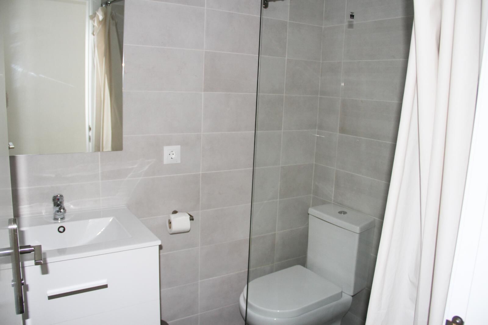 Un baño con lavamanos, inodoro y ducha blancos.