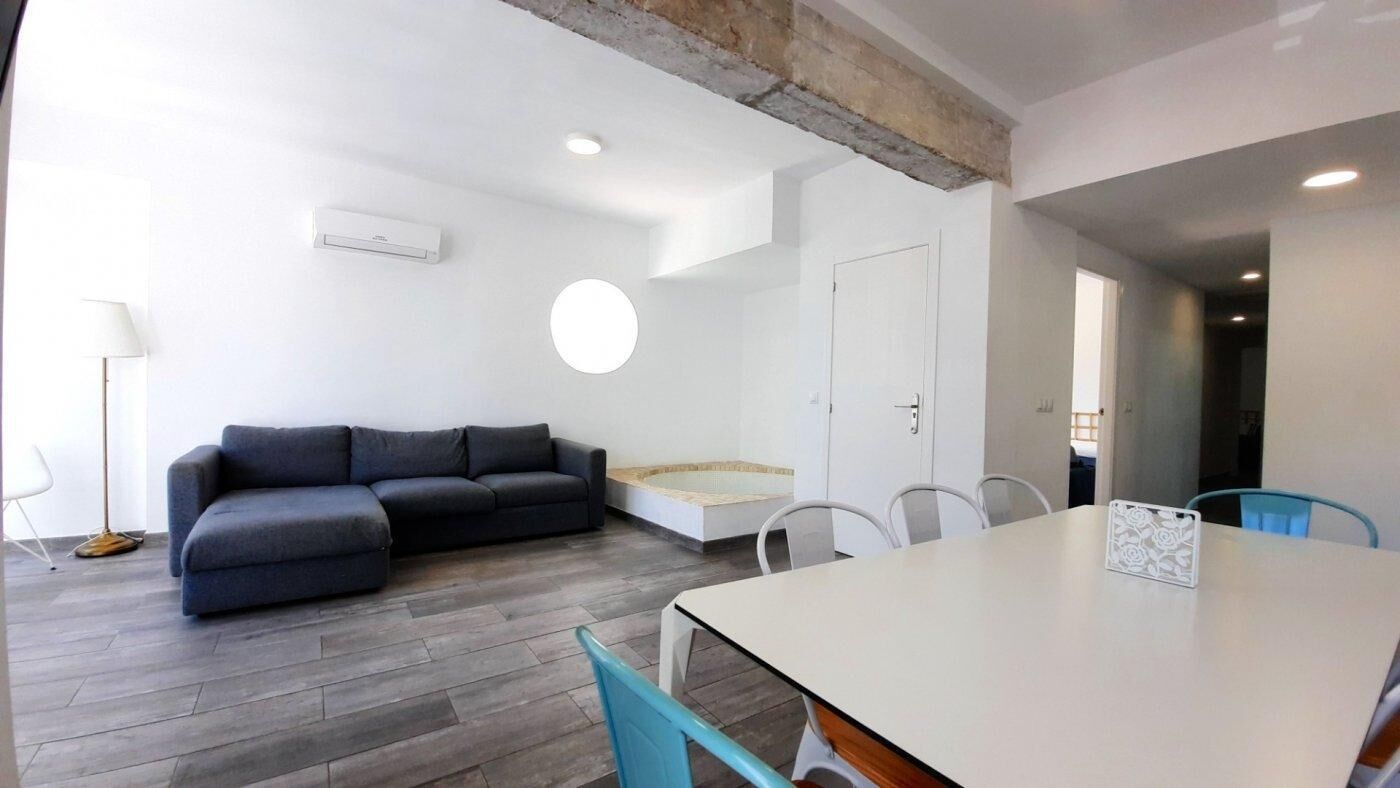 Una sala de estar moderna con un sofá gris, una mesa de comedor con sillas y una ventana redonda pequeña.