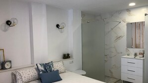 A modern bedroom with a bed, bedside tables, a nightstand, a mirror, and a bathroom with a shower and sink. - Loft 20 meters from the sea D13 (Gandia)