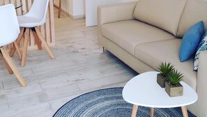 A modern living room with a beige sofa, white chairs, a small round coffee table with plants, and a patterned rug. - Loft 20 meters from the sea D13 (Gandia)