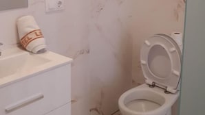 A bathroom with a marble wall, a white toilet, a sink with a towel, and a glass shower enclosure. - Loft 20 meters from the sea D13 (Gandia)