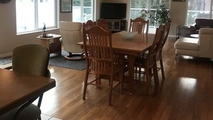 A spacious living room with a dining area, large windows, a ceiling fan, and a TV. -  ORCA HOUSE SPECTACULAR VIEW!! KACHEMAK DRIVE (Homer)