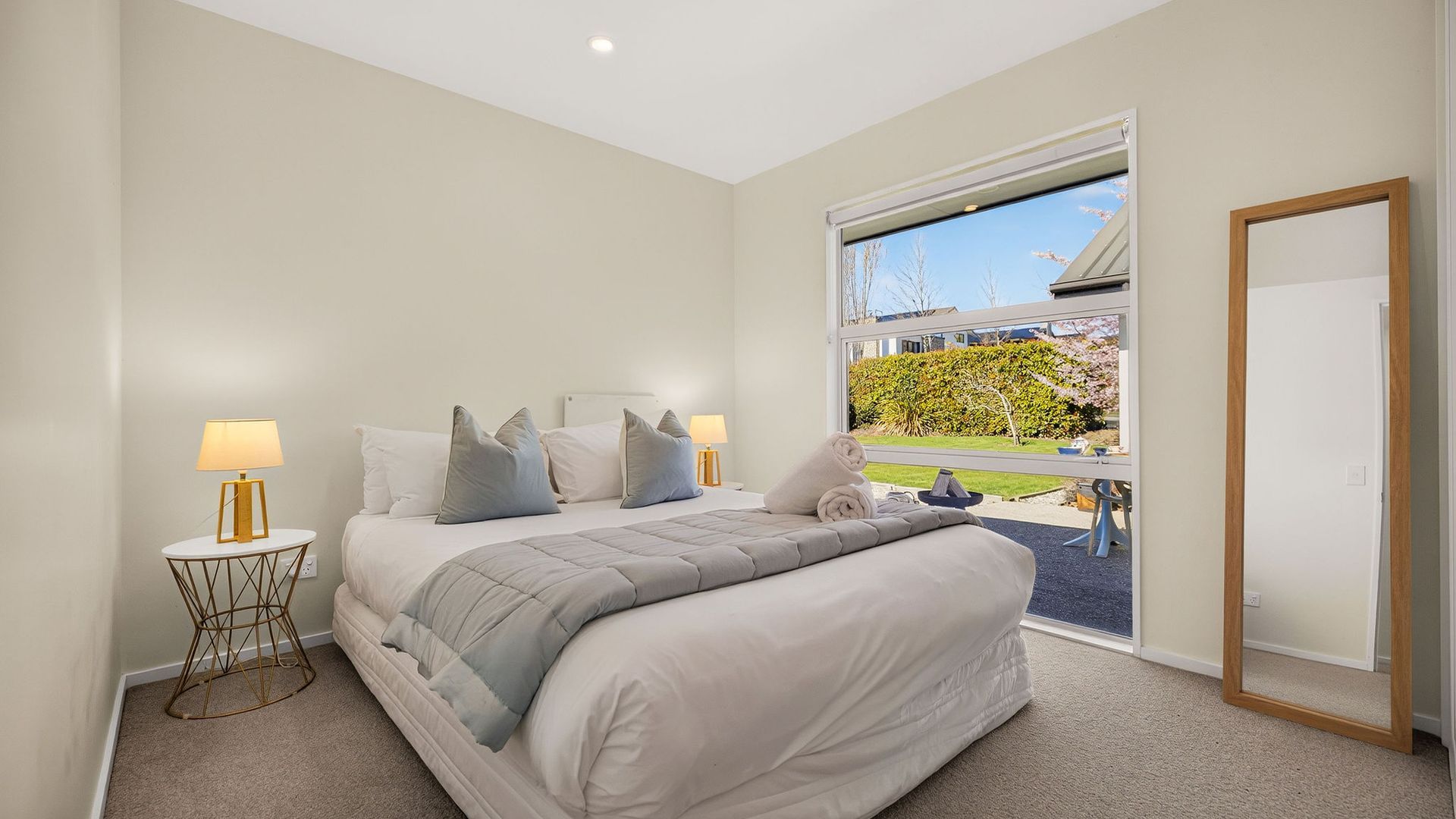 A bedroom with a bed, bedside lamps, a window with a view of the outdoors, and a mirror.