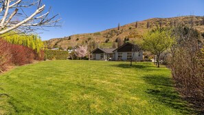Een woonhuis met een verzorgd gazon, twee huizen en een heuvelachtig landschap op de achtergrond.