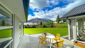 A modern outdoor patio with a table and chairs, a view of a mountain, and a well-maintained lawn. - Apple Tree Cottage - Just minutes from Queenstown Central (Queenstown)