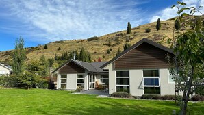 A modern two-story house with a sloped roof, large windows, and a well-maintained lawn. - Apple Tree Cottage - Just minutes from Queenstown Central (Queenstown)