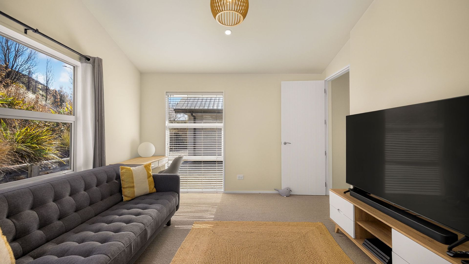 A modern living room with a grey sofa, a flat-screen TV, and a large window.