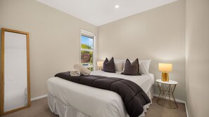 A hotel room with a bed, a bedside table with a lamp, and a window with a view of greenery.