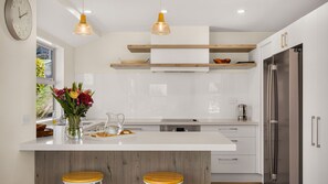 Een moderne keuken met een centraal eiland, houten krukken, een roestvrijstalen koelkast en hanglampen.