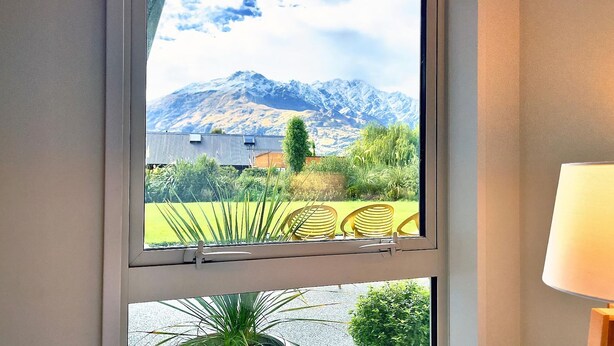 A window with a view of a mountain, a grassy area, and a building with a sloped roof. - Apple Tree Cottage - Just minutes from Queenstown Central (Queenstown)