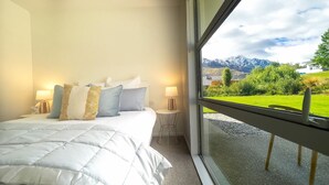 A bedroom with a bed, pillows, bedside tables, and a window with a mountain view. - Apple Tree Cottage - Just minutes from Queenstown Central (Queenstown)