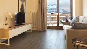 A modern living room with a TV, a framed deer picture, a plant, and a balcony with a mountain view. - Splendid 4+2 attic with panoramic terrace overlooking the mountains (301) (Lavarone)