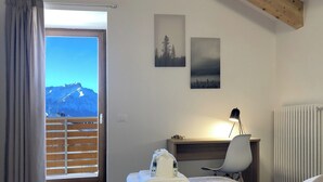 A hotel room with a bed, a desk, a chair, a radiator, and a view of mountains. - Splendid 4+2 attic with panoramic terrace overlooking the mountains (301) (Lavarone)