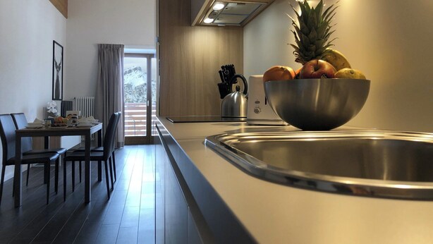 A modern kitchen with a stainless steel sink, wooden ceiling beams, and a dining area with a table and chairs. - Splendid 4+2 attic with panoramic terrace overlooking the mountains (301) (Lavarone)