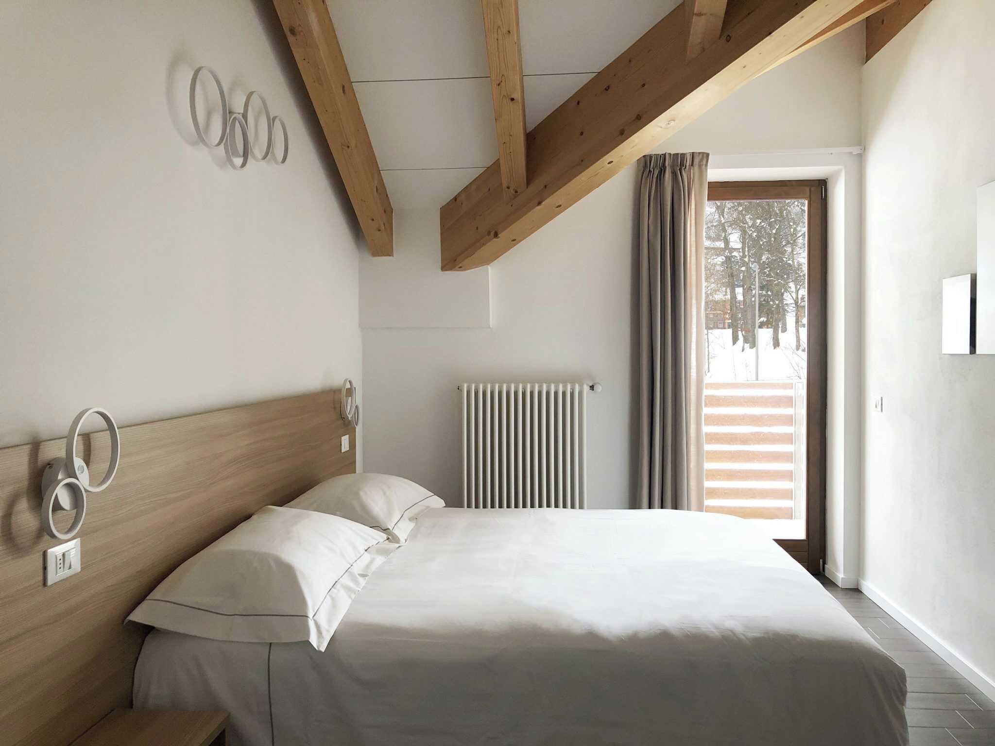 Ein Schlafzimmer mit Holzboden, einem Bett mit weißer Bettwäsche, einem Heizkörper und einem Fenster mit Vorhängen.