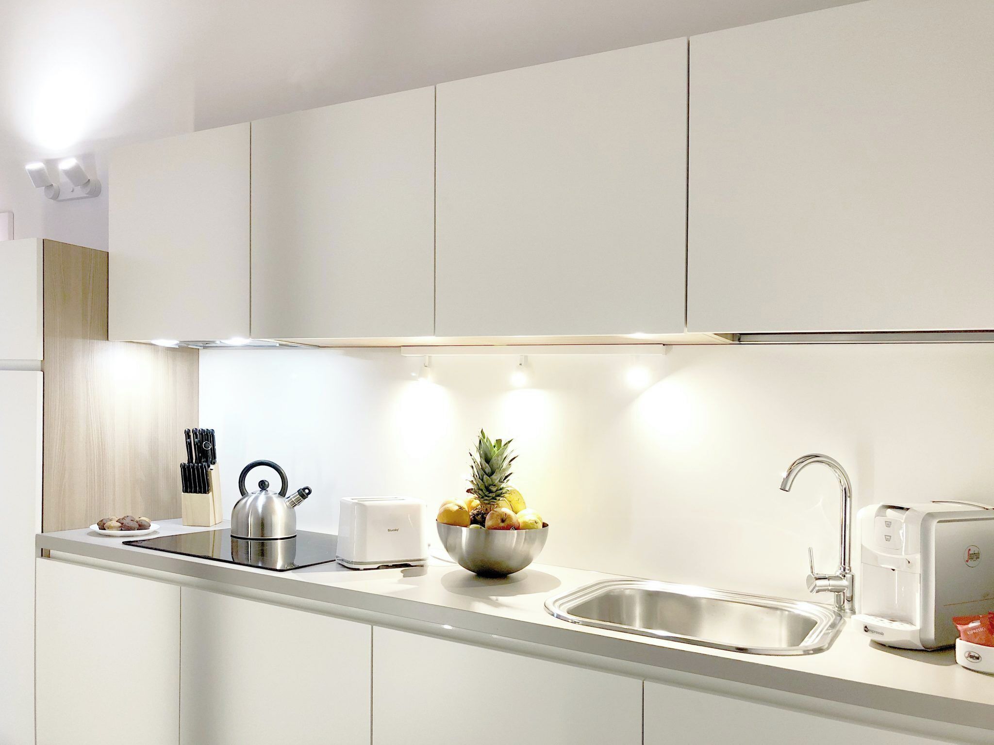 Een moderne keuken met witte kasten, roestvrijstalen apparatuur en een fruitschaal op het aanrecht.
