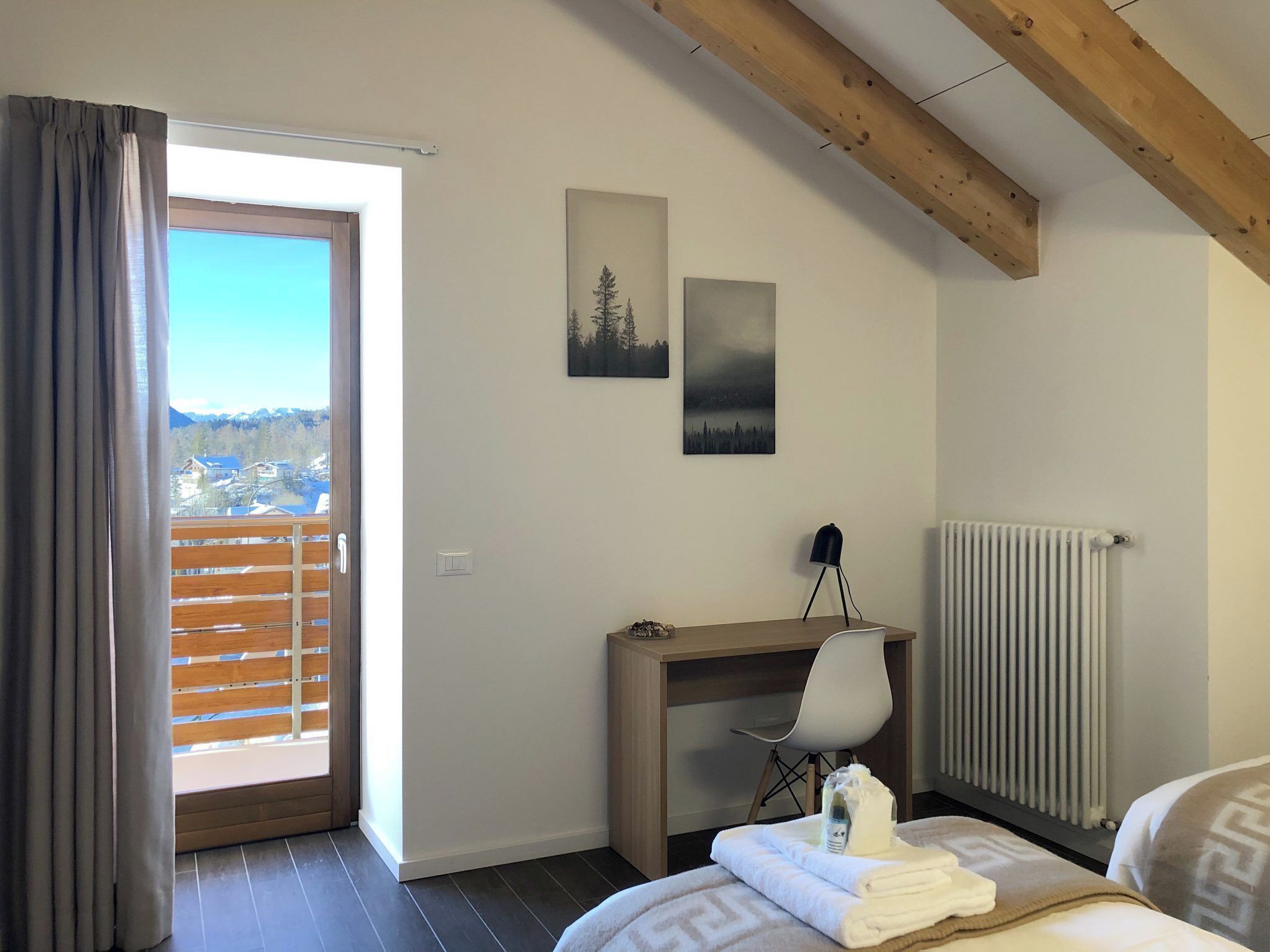 A bedroom with a bed, a desk, a chair, a radiator, and two paintings on the wall.