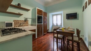 A kitchen with a gas stove, microwave, and wooden cabinets. There is a dining table with chairs and a window with curtains. - San Lorenzo Cozy and Comfortable Flat (Rome)