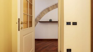 An open door leading to a room with a wooden floor, a stone archway, and a shelf with a bowl. - San Lorenzo Cozy and Comfortable Flat (Rome)