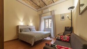 A bedroom with a bed, a sofa, a chair, and a window with curtains. - San Lorenzo Cozy and Comfortable Flat (Rome)