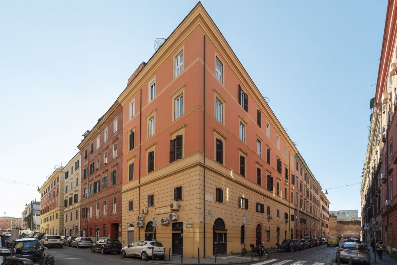 A multi-story building with a corner entrance, multiple windows, and parked cars along the street.