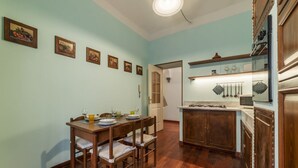 A dining area with a wooden table and chairs, a kitchen with wooden cabinets, and a light blue wall with framed pictures. - San Lorenzo Cozy and Comfortable Flat (Rome)