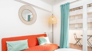 A bright living room with a red sofa, a round mirror, and a floor lamp. - Appartement Corail - Welkeys (Antibes)